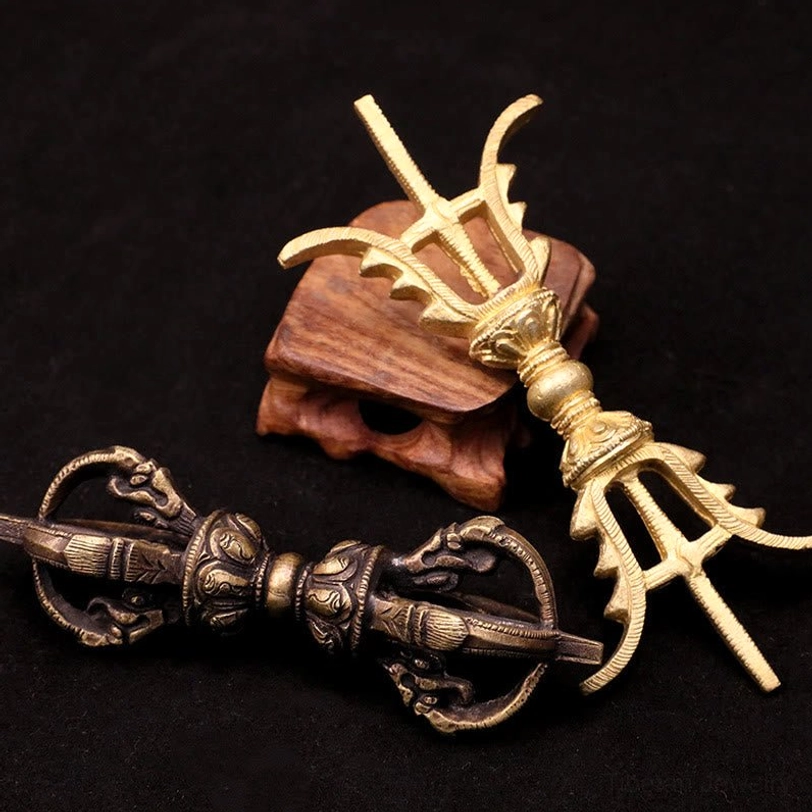 Tibetan Vajra Dorje three-prong and five-prong styles side by side on wooden display stand, showing antique brass and bronze finishes with aged patina