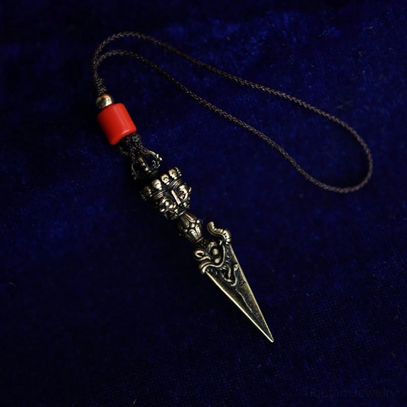 Tibetan Dorje Vajra hanging necklace with wax cord and red accent bead, bronze-toned metal side view on blue velvet background