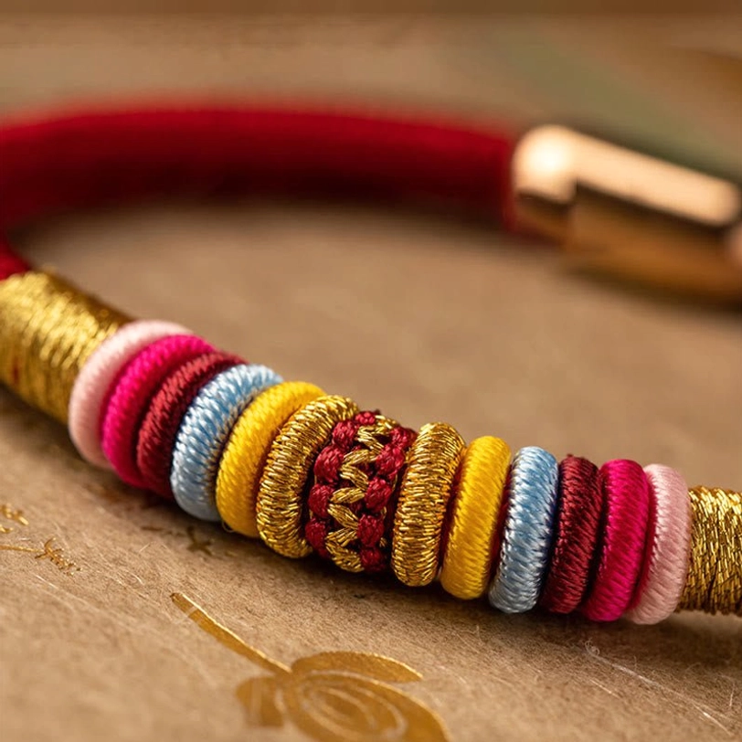 Close-up macro detail of Tibetan Vajra Knot bracelet showing multi-color woven wraps and gold thread decoration