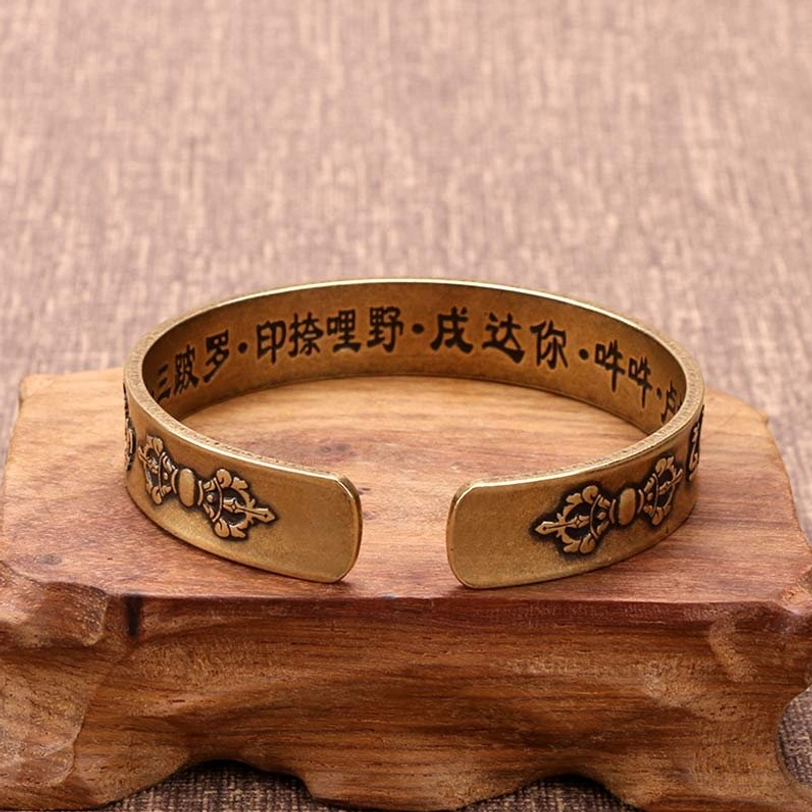Tibetan Vajra mantra cuff bracelet overhead view with embossed Vajra patterns and Chinese sutra on wooden stand