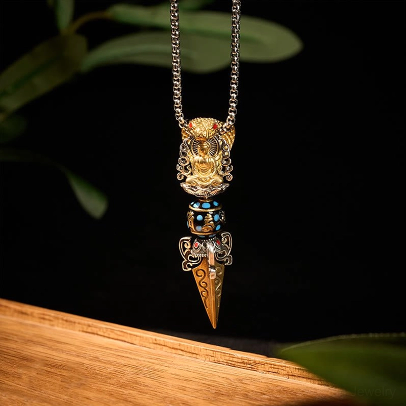 Sacred Tibetan Buddhist Vajra pendant hanging vertically showing intricate enamel bead detail, pointed spike, and gold-silver dual tone finish on wooden surface