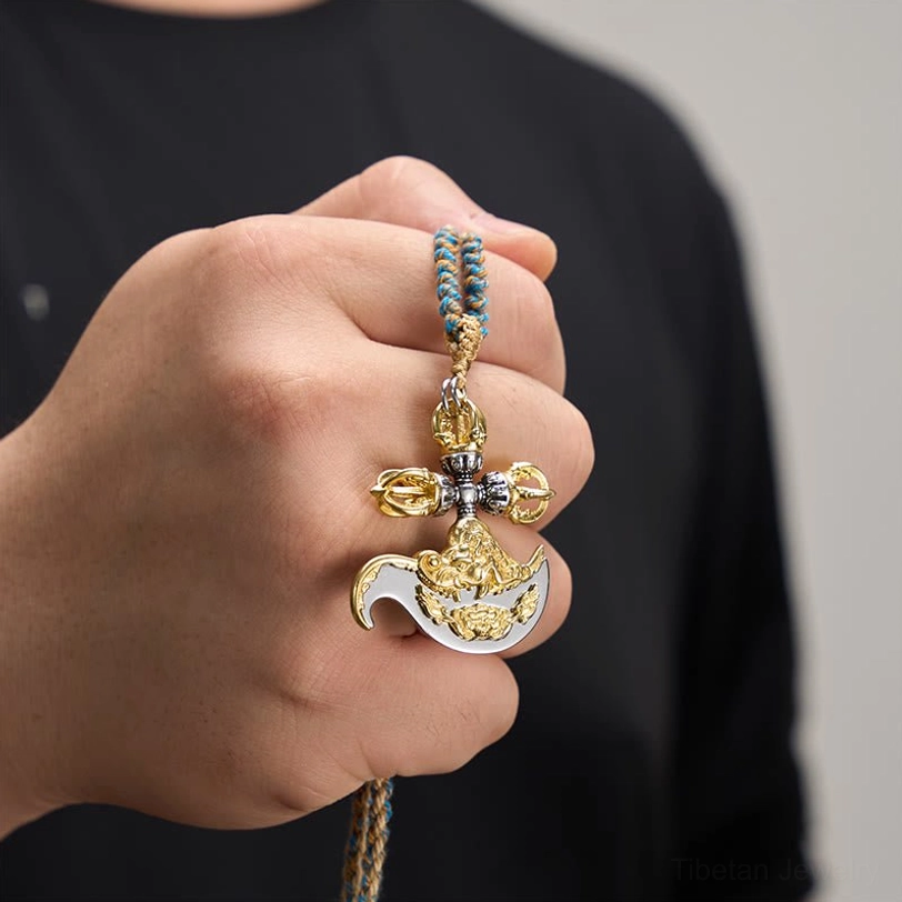Person wearing copper vajra pendant necklace on hand, first-person perspective showing dual gold and silver metal with colored braided rope against black clothing