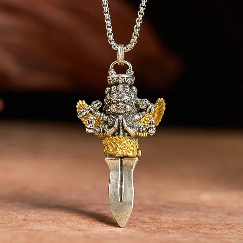 Overhead front view of Tibetan Vajra necklace pendant with clear multi-arm deity design, silver and gold dual-tone finish on light wooden surface