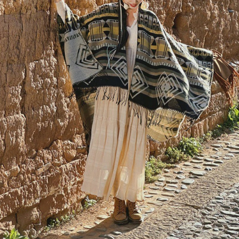 Vintage geometric tassel shawl with tribal prints, styled with beige long dress, adobe clay wall background, bohemian aesthetic