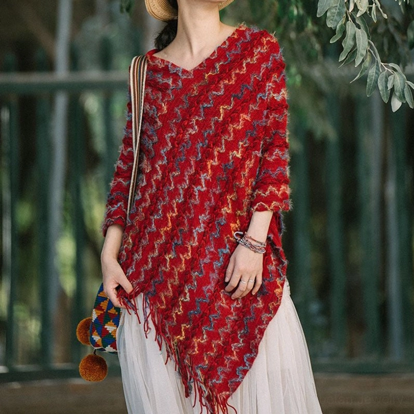 V-neck tibetan ethnic knit poncho in red-based multicolor weave with bracelet accessory on outdoor green foliage background