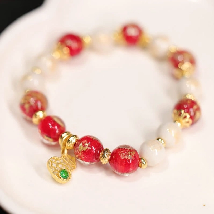Tibetan prosperity bracelet with heart-shaped gold filigree pendant, mixed red white and gold liuli glass beads arranged on white ceramic plate
