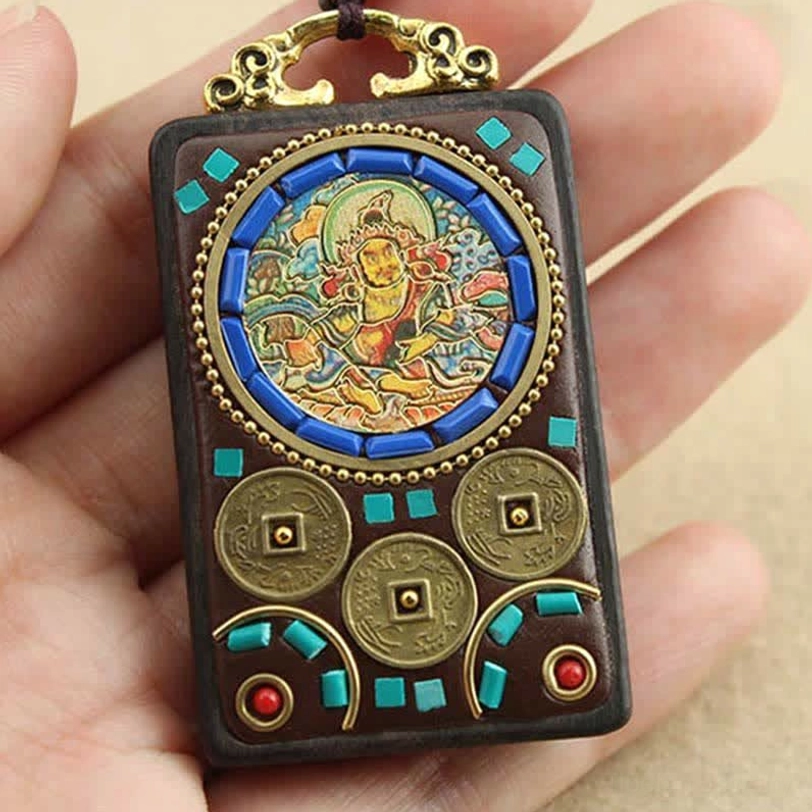 Close-up of Tibetan wealth god thangka pendant held in hand showing intricate artwork, ebony wood and ornate metal bail
