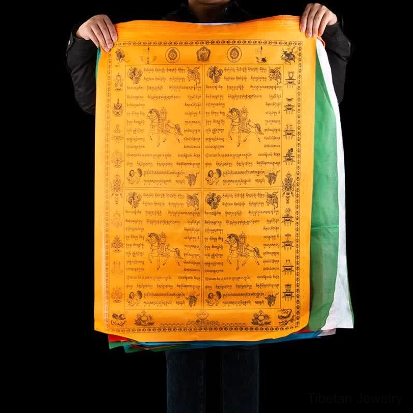 Tibetan windhorse prayer flag held in hands featuring bright orange base with black printed Buddhist iconography and colorful side borders