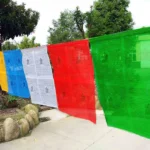 Tibetan five color windhorse prayer flags hanging outdoors in garden pathway with blue white red green yellow fabric printed with Buddhist scriptures