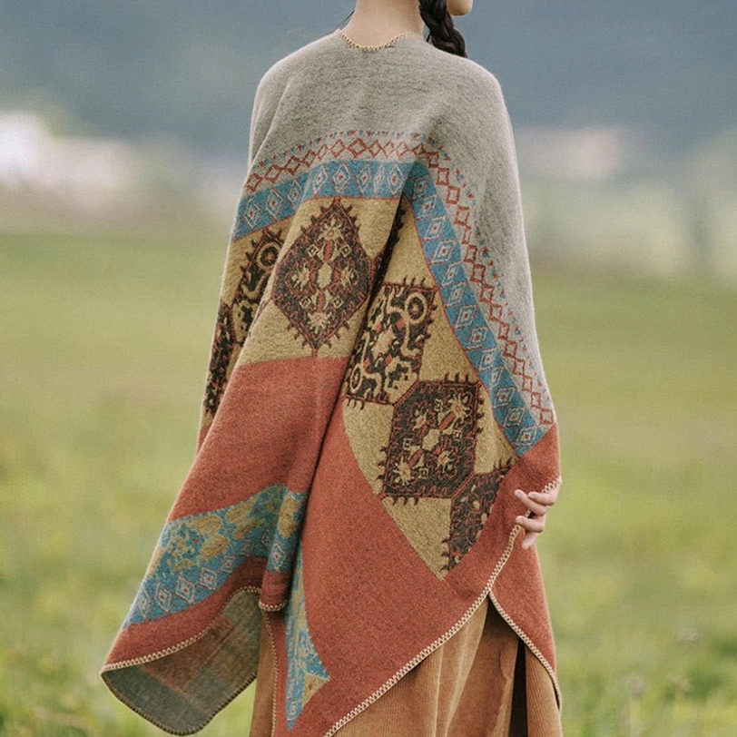 Ethnic style winter poncho back close-up detail with jacquard pattern showing terracotta and blue color blocks on grassland