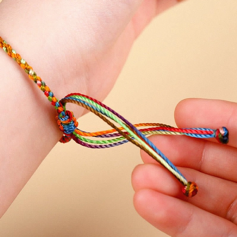 Hand-knotted rainbow braided protection bracelet close-up showing silk-like cord texture and adjustable trailing rope