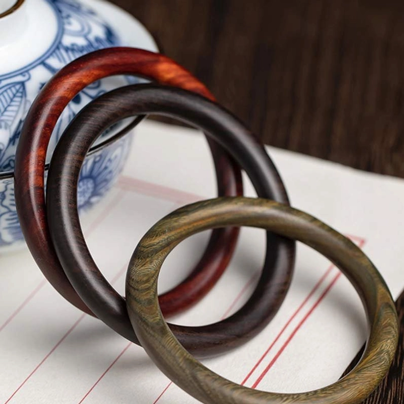 Set of three Tibetan wood protection bracelets in different materials - red sandalwood, ebony, and green sandalwood - flat lay with vintage porcelain