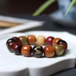Om Mani Padme Hum wooden mala bracelet in mixed natural wood with engraved Sanskrit mantra bead on white ceramic tray