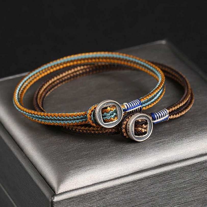 Dual tibetan silver protection bracelets with matching woven cords and engraved silver button clasps on jewelry storage box