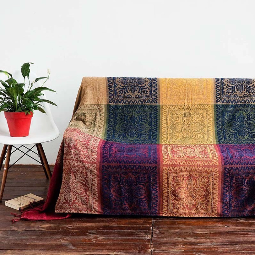 Tibetan artisan blanket draped on modern couch with symmetric damask patterns in muted earthy tones and side table styling