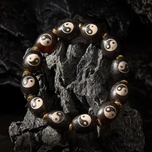 Oblique angle view of Tibetan protection bracelet displaying intricate Yin Yang etching on dark polished agate beads with brass accents