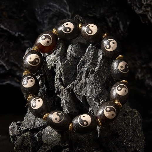 Oblique angle view of Tibetan protection bracelet displaying intricate Yin Yang etching on dark polished agate beads with brass accents
