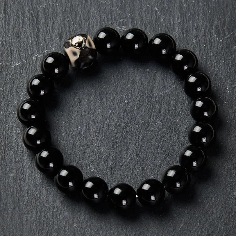 Black stone Yin Yang bracelet with polished round beads and metallic charm on slate background