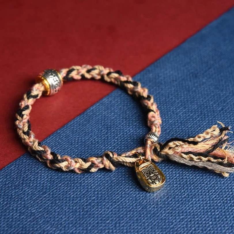 Two-tone tan khaki Tibetan Zakiram bracelet side view showing woven cord gold carved pendant silver engraved bead and tassel ends