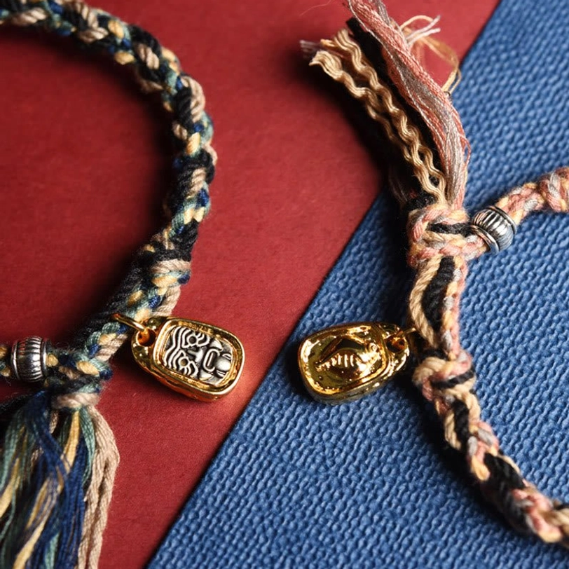 Two distinct Tibetan Zakiram bracelets dark cord and tan cord with matching gold pendants frayed tassels and silver hardware