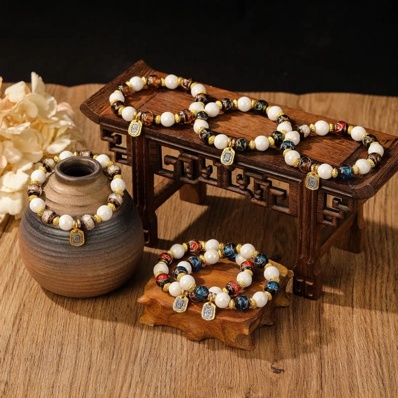Tibetan charm bracelets with glazed porcelain beads and engraved metal pendants displayed on vintage wooden surface