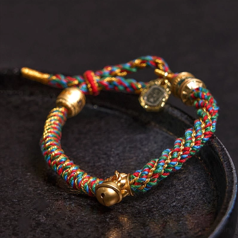 Close-up side view of handmade Tibetan Buddhist amulet bracelet featuring twisted rainbow cord, gold-tone hardware, and engraved charm beads