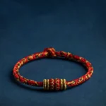 Handmade Tibetan red string zodiac natal Buddha luck bracelet with gold accents on dark blue background
