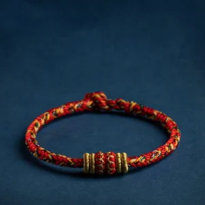 Handmade Tibetan red string zodiac natal Buddha luck bracelet with gold accents on dark blue background