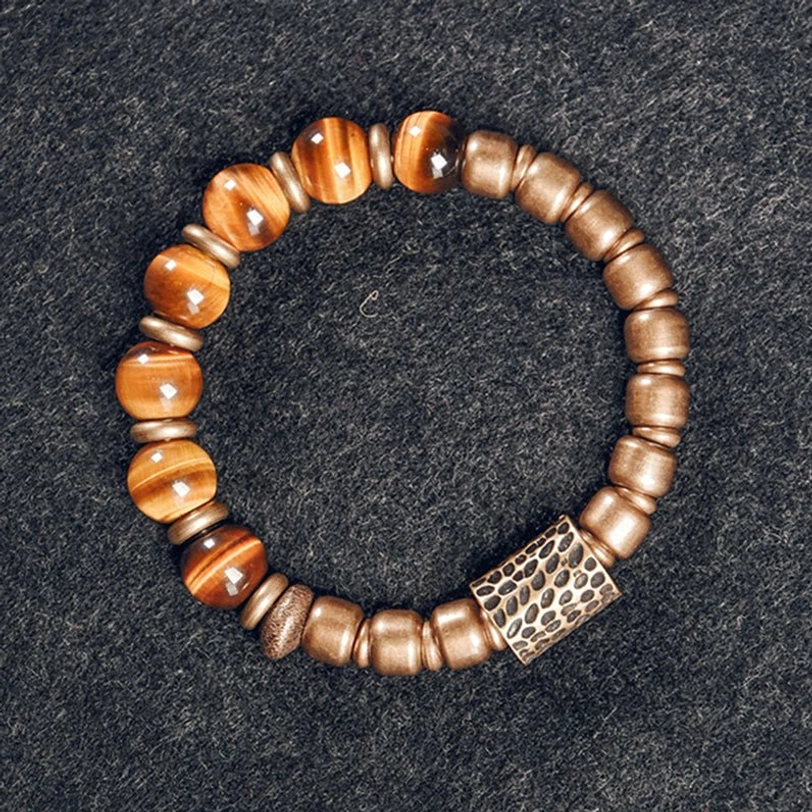 Polished tiger eye stone beads with rectangular hammered copper accent, top-down view on dark wool