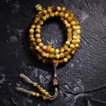 108-bead Tiger Eye mala bracelet flat lay with copper Vajra guru bead and tassel counter on dark textured stone background