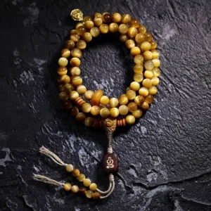 108-bead Tiger Eye mala bracelet flat lay with copper Vajra guru bead and tassel counter on dark textured stone background