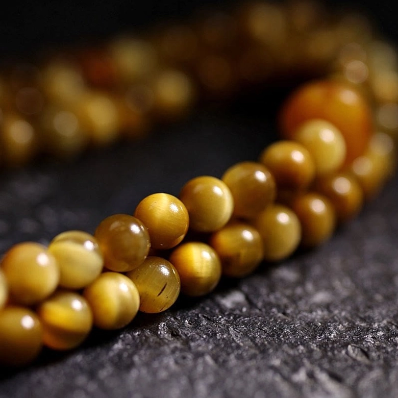 Smooth round Tiger Eye beads in warm golden-brown hue with shallow focus close-up photography on dark stone