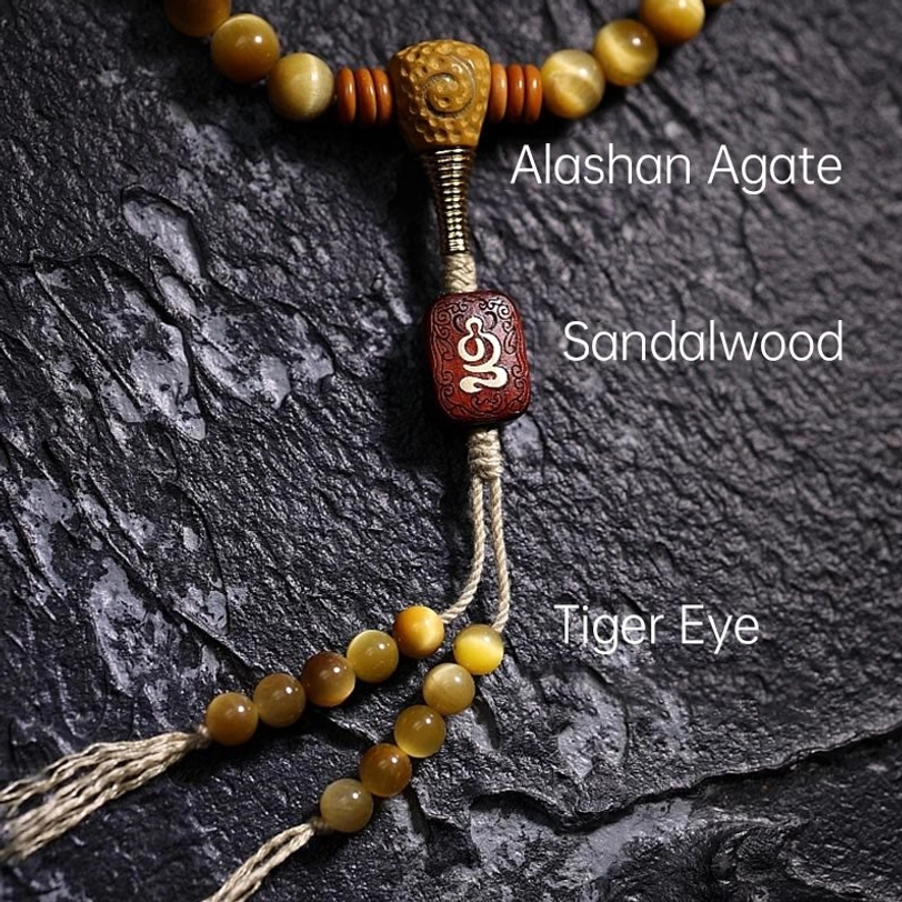 Guru bead section of Tiger Eye mala featuring labeled natural stone materials, copper Vajra dorje, and sandalwood pendant
