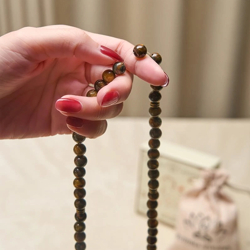 Tiger eye stone mala held in hand with red nail polish, branded Buddha Stones pouch visible in background