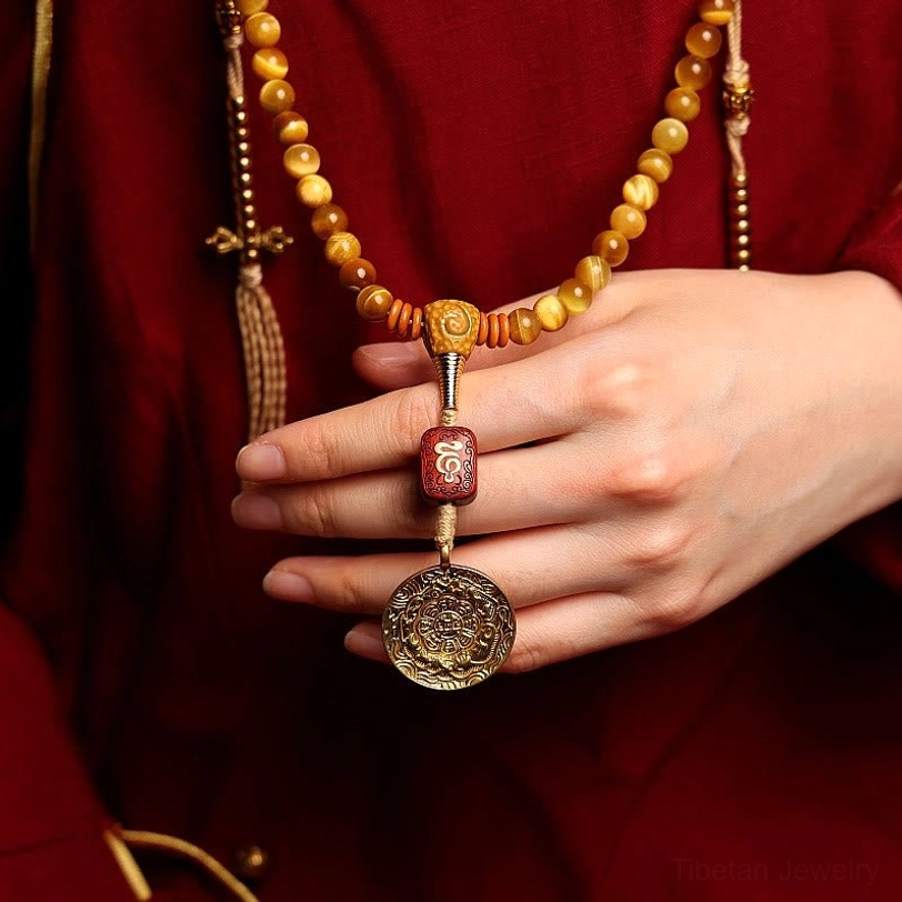 Tiger Eye mala necklace worn close-up with dangling metal medallion and bead strand against red traditional clothing