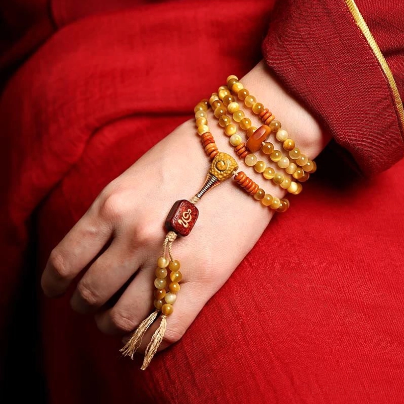 108-bead Tiger Eye mala bracelets layered and worn on wrist with carved wooden pendant charm against red traditional Tibetan robe