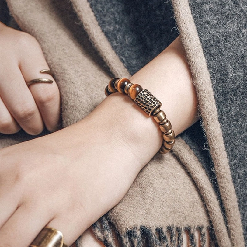 Natural tiger eye bracelet stacked on wrist with tan woolen scarf, showing cylindrical copper spacer