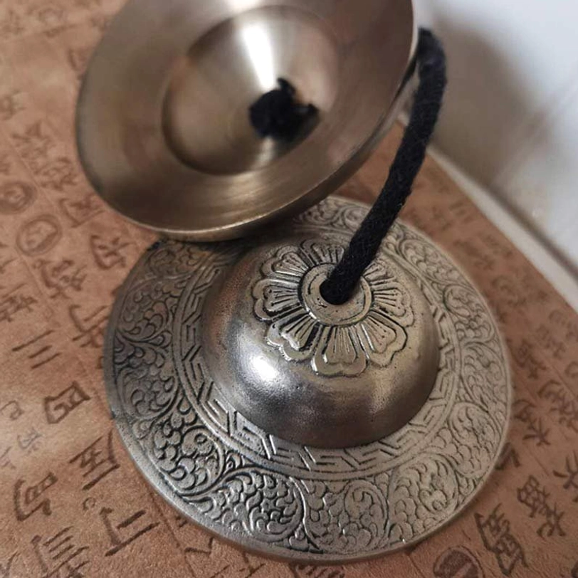 Single Tibetan tingsha cymbal close-up side view embossed floral center engraved border
