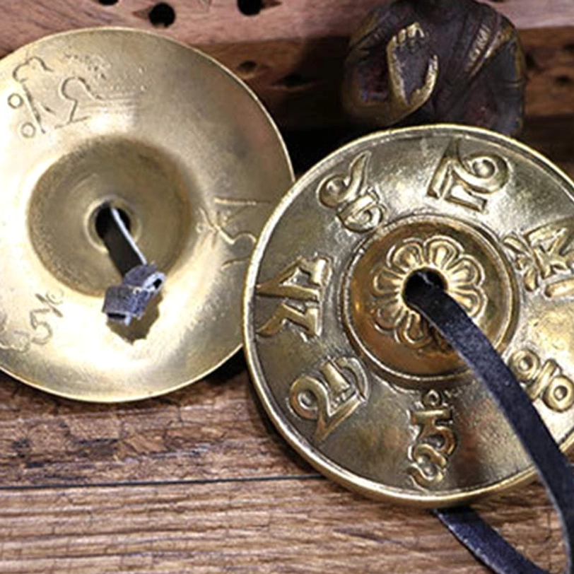 Tibetan tingsha cymbals overhead view showing both bell sides with floral center engraving and complete mantra inscriptions on wooden table