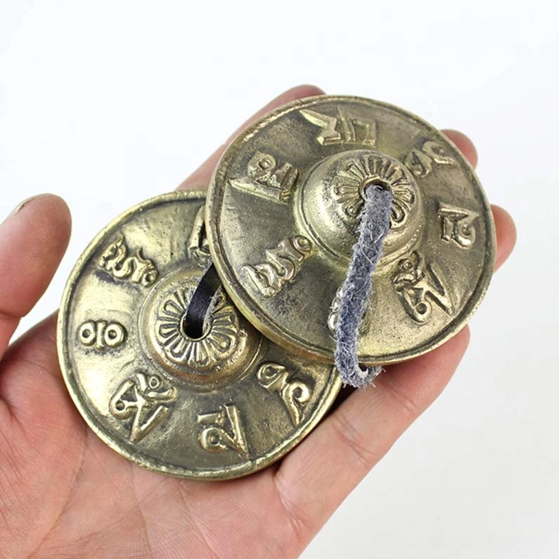 Pair of brass tingsha bells held in palm showing full view of both cymbals with mantra engravings