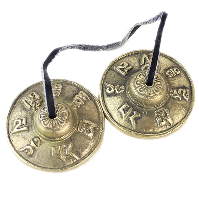 Tibetan tingsha bells pair connected by leather cord showing one engraved and one plain surface on white background