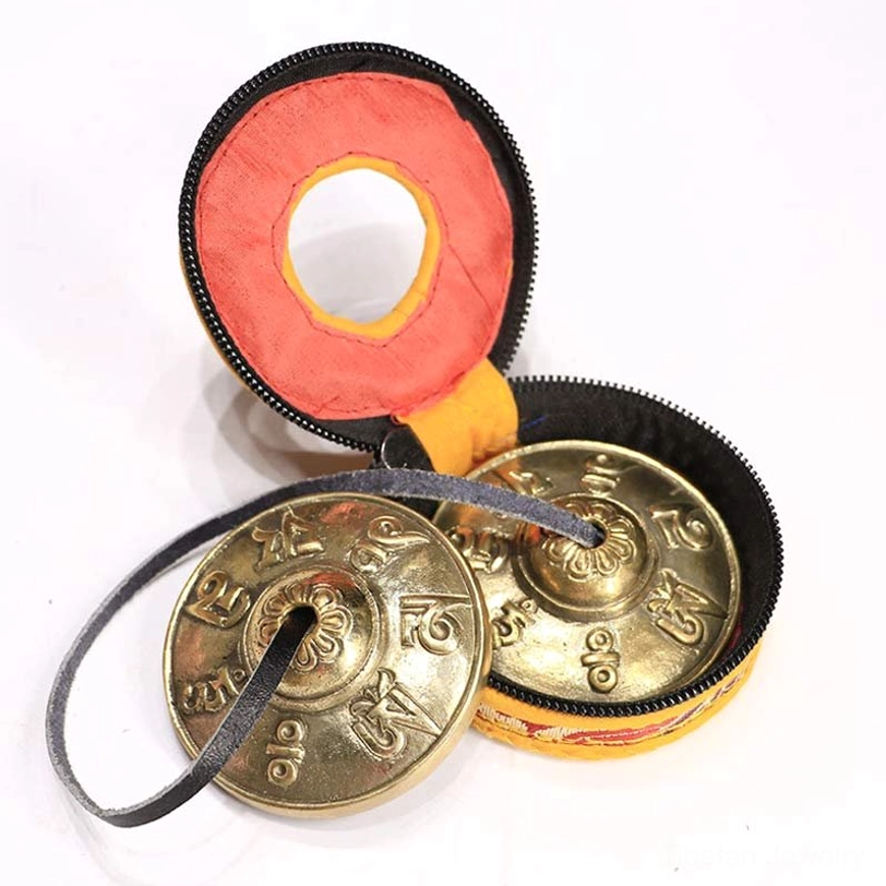 Tibetan tingsha bells with protective embroidered fabric pouch and leather carrying strap on white background