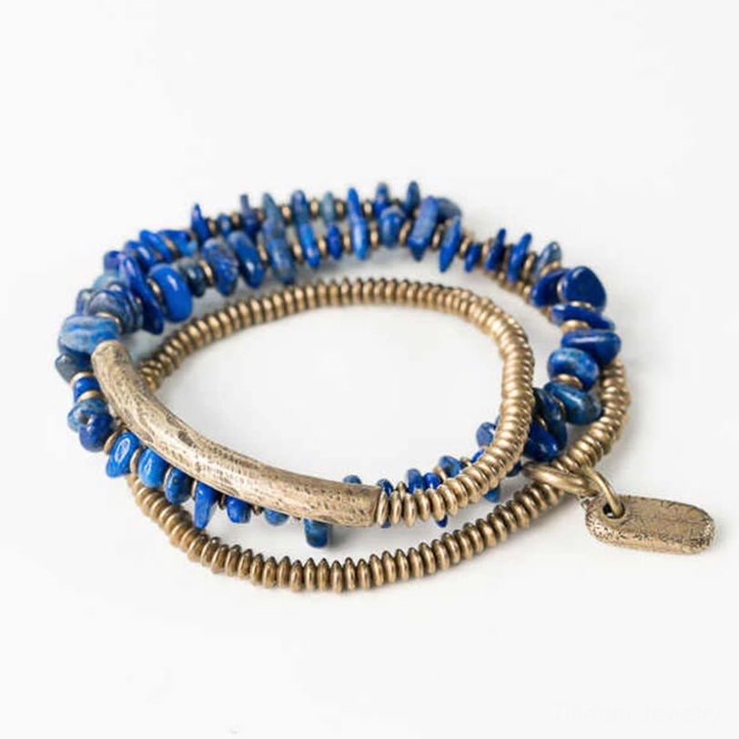 Top-down view of lapis lazuli triple wrap bracelet with brass tube and mixed bead strands on white background
