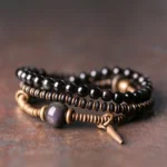 Triple wrap rainbow obsidian healing bracelet with ebony wood and copper accents, overhead view on dark rustic surface