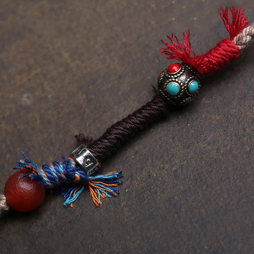Close-up macro view of turquoise dzi bead necklace end with red agate and fringed knot decoration