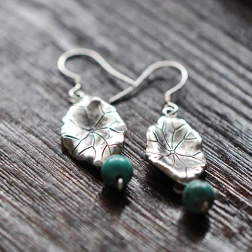 Flat lay overhead view of polished silver lotus leaf turquoise drop earrings on dark wooden tabletop