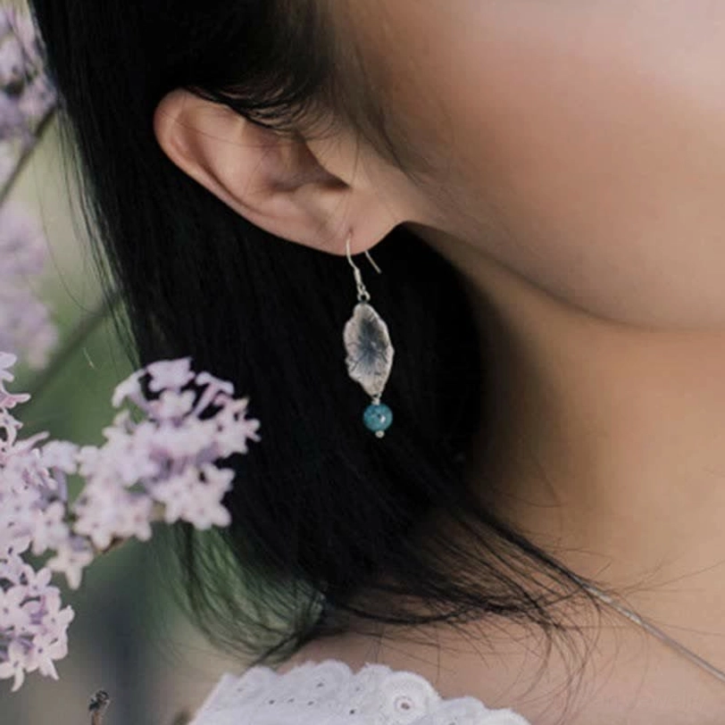 Female model wearing turquoise lotus leaf drop earrings in profile with lilac flower background
