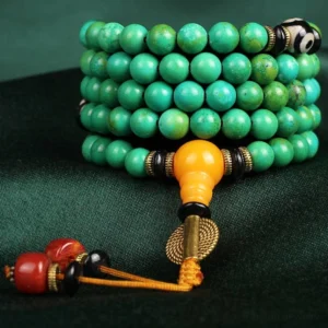 Close-up side view of stacked turquoise prayer beads mala with Dzi accents and amber-colored guru bead on dark velvet fabric