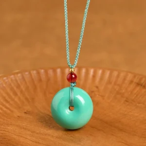 Turquoise peace buckle pendant necklace flat lay showing donut-shaped turquoise stone with teal woven cord and red accent bead on wooden background
