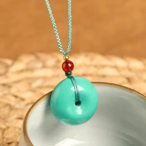 Overhead view of turquoise peace buckle tibetan necklace with gold spacer bead and red decorative bead on ceramic bowl background